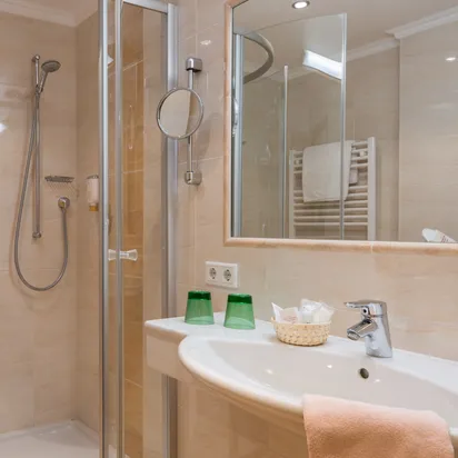 Modern hotel bathroom with glass shower, large mirror, and sink with amenities